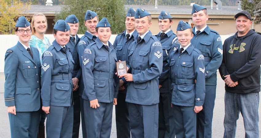 A group of cadets and adults in uniform, standing together and smiling, holding a small plaque.